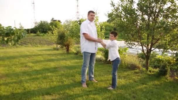 Pai e filho caminham juntos no jardim verde perto da casa. — Vídeo de Stock