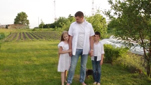 Papai e duas crianças caminham juntas no jardim verde perto da casa. — Vídeo de Stock