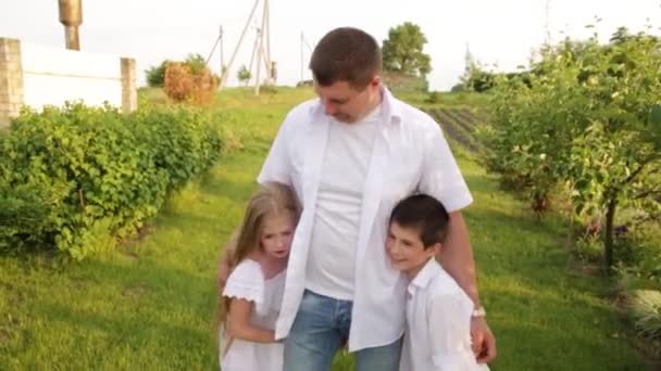 Pappa och två barn går tillsammans i den gröna trädgården nära huset. — Stockvideo