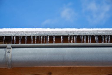 Kışın yağmur oluğu ile Çatı. Kar ve buz sarkıtlı çatı.