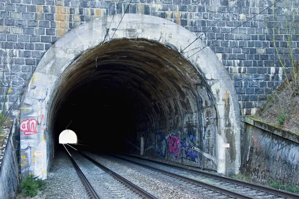 Çift hatlı demiryolu tüneli. Demiryolu altyapısı. Tünelin sonundaki ışık. Graffity ile boyanmış eski taş tünel. — Stok fotoğraf