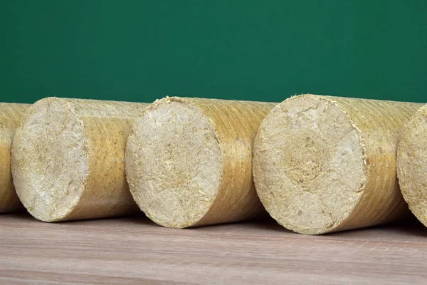 Wood sawdust eco-briquettes straightened, green background. Alternative fuel, bio fuel — Stock Photo, Image