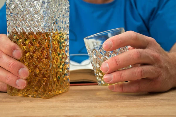 Kristal dekantörde alkollü içki. Adam elinde viski içeceği bir bardak tutar. Gözlüklü açık kitap.