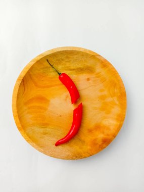 Kırmızı biberin tamamı ortadan kesilmiş, ahşap bir tabakta servis edilmiş, beyaz bir arka planda izole edilmiş..