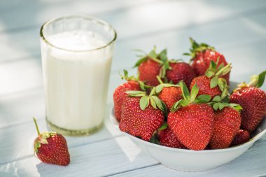 Olgun çilek ve bir bardak süt hafif bir arka plan üzerinde. Doğal basit gıda.