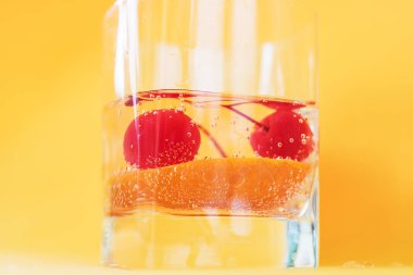Bir cam bardak soğuk içecek yakın çekim. Kiraz ve gaz kabarcıkları turuncu bir dilim.