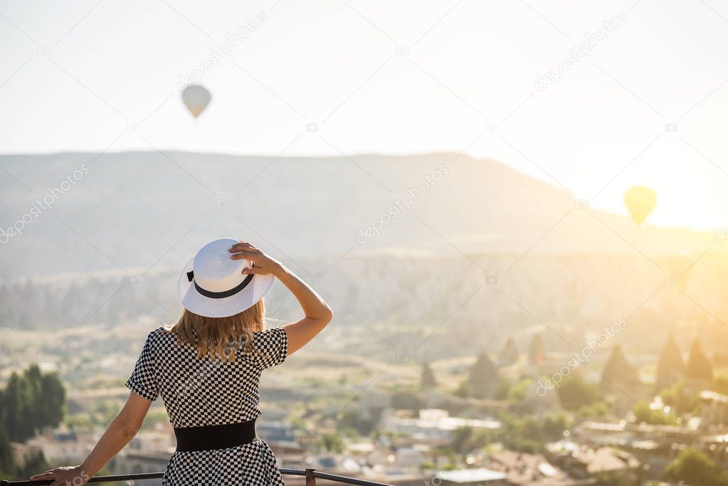 The girl standing on the terrace and staring into the distance on the balloons in the sky. Turkey. Cappadocia.