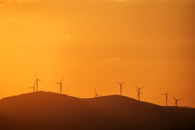 Rüzgar jeneratör dağ doruklarına günbatımı, silüetler, bir tepe üzerinde.