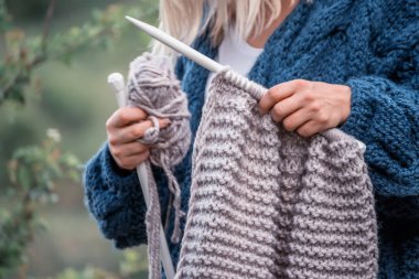 Bir kız büyük örgü iğne ve iplik skein elleri. Bir kız bahçede örme pürüzlü ceket.