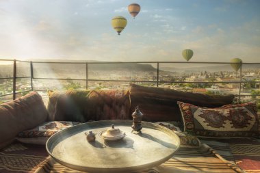 Rahat bir teras çatı ve tarihi kent merkezine ve sabahın erken saatlerinde hava balonları bir görünümünü oryantal yastık ile. Türkiye. Cappadocia. Göreme Milli Parkı.