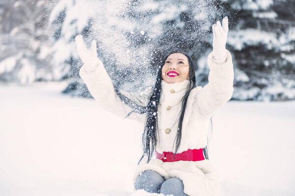 A girl in a forest glade among the trees in the snow throws snow into the air. Funny winter days.