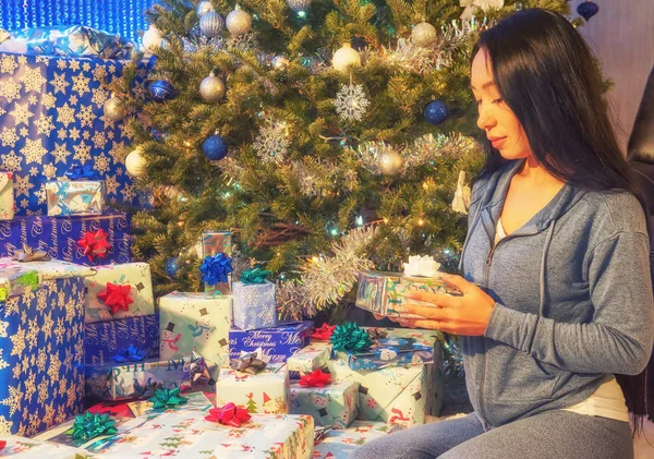 A girl in simple home clothes with a mountain of presents at a Christmas tree