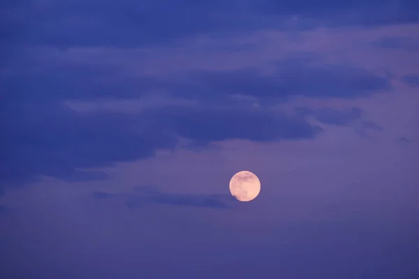 A full moon among the clouds in the sky.