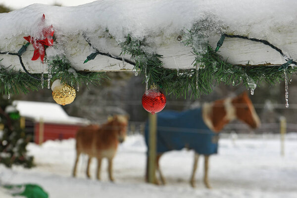 A wooden fence on a farm decorated with New Year's Christmas toys and garlands and horses. . USA. Maine.