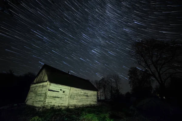 Old wooden hut and the Milky Way. Night photo. Star tracks in the sky.