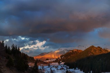 Ladin ormanı arasında vadide dağlar ve küçük evler de şaşırtıcı güzel gün batımı. Kış, ilkbahar manzarası. Romanya.