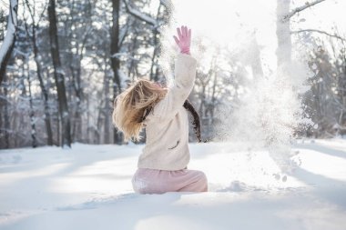 Neşeli kız kış ormandaki düşme karda eğleniyor.