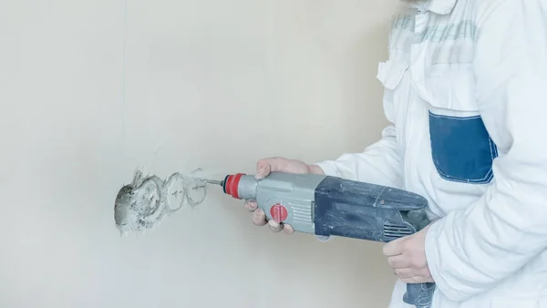 A man drills a wall with a perforator. A man works with construction tools.