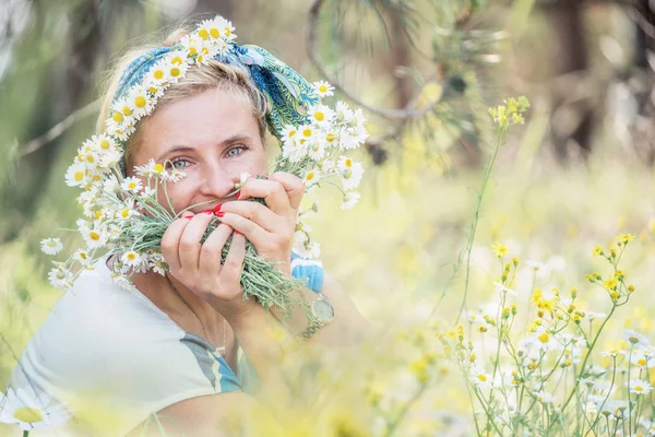 Happy simple woman on a summer meadow with a bouquet of daisies and a wreath of daisies.