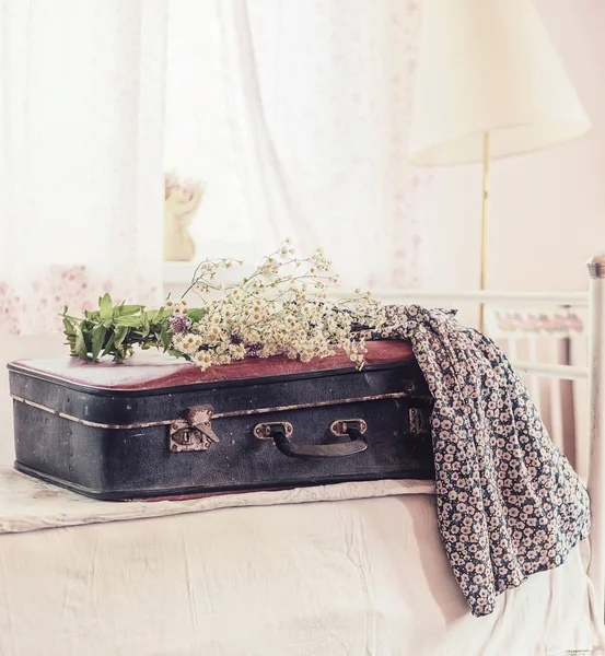 An old suitcase, a bouquet of wildflowers and a simple dress on an old bed. Vintage style, retro photo.