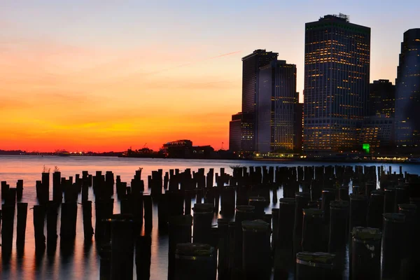 日没時のニューヨークの夜市中心部にある湾の水からの眺め 夕焼けの空に暗闇の中で輝く超高層ビル — ストック写真
