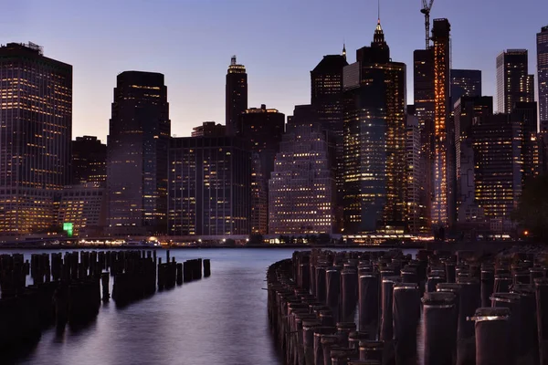 日没時のニューヨークの夜市中心部にある湾の水からの眺め 夕焼けの空に暗闇の中で輝く超高層ビル — ストック写真