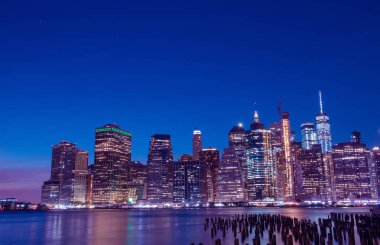 Gün batımında New York'un gece şehir merkezinde körfezin suyundan görünümü. Gün batımı gökyüzüne karşı karanlıkta parlayan gökdelenler.