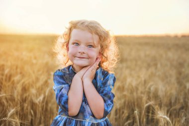 Hafif güneş ışığında altın bir buğday alanında küçük sevimli kıvırcık saçlı kırmızı saçlı kız.