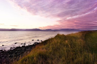Gün doğumunda Körfez kıyısı. Şafak ışığında dağların siluetleri. İzlanda. Su yakınında sabahın erken saatlerinde ıssız güzel manzara.