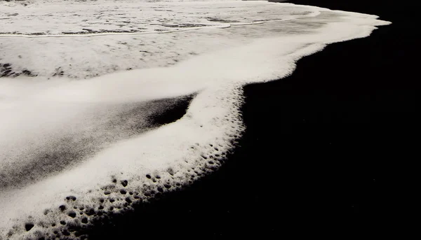 Black volcanic sand and white foam sea wave. Closeup of a natural landscape. Minimalism of lines and colors.