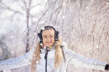 Kız güzel bir kış parkında eğleniyor. Ağaç dalları büyülü köpüklü buz ve kar ile kaplı. Kız eğleniyor ve kar atıyor.