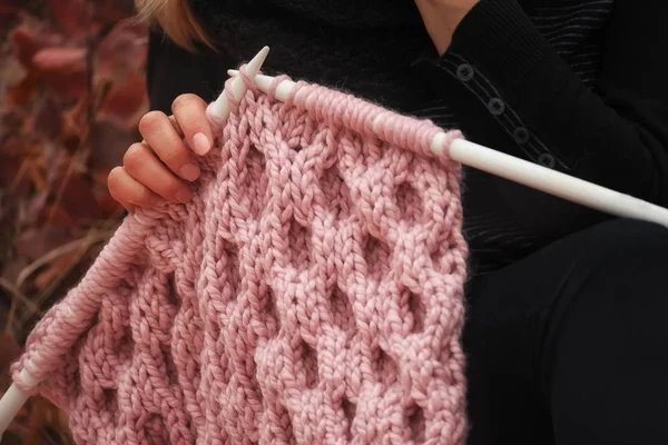 Knitting on knitting. Hands close-up knitting on knitting needles, pink wool knit against the backdrop of a natural garden. Needlework in the garden.