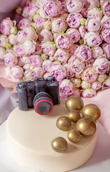 Cake with a chocolate figurine and a bouquet of pink peony roses. Congratulations on Photographer\'s Day.