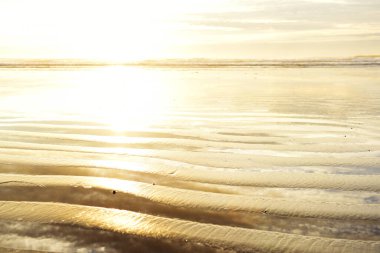 Dalgalar alçaldığında ve şafak söktüğünde okyanusta kabartmalı altın rengi kum. Okyanusta altın gün doğumu.