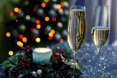 İki kadeh köpüklü şarap, bir Noel çelengi ve arka planda yılbaşı ağacı ışıkları. ev kış tatili atmosferi 