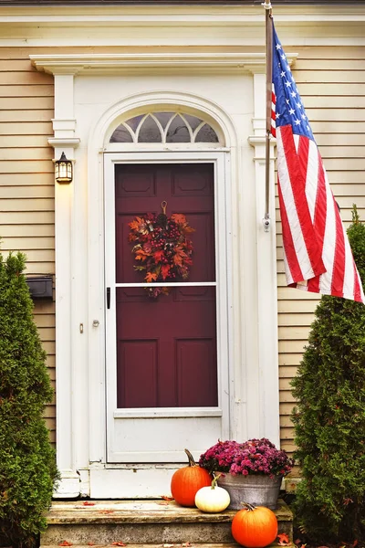 Pumpkins and autumn flowers at the door of an old house and an American flag. USA. Maine.
