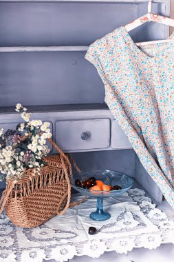 Eski moda natürmort hayat. Hasır bir çanta ve bir buket çiçek eski bir büfenin arka planında çiçekler olan bir elbise. seçici yumuşak odak.