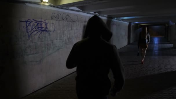 Hombre con capucha persiguiendo a mujer en túnel oscuro — Vídeos de Stock
