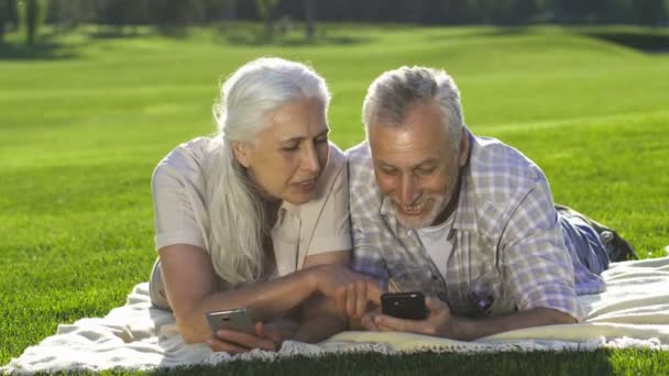 Casal sênior usando telefones celulares deitados no gramado — Vídeo de Stock