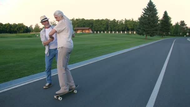 Чоловік навчає дружину скейтборді в літньому парку — стокове відео