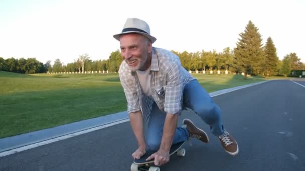 Vrolijke oudere man skateboarden op knie in park — Stockvideo