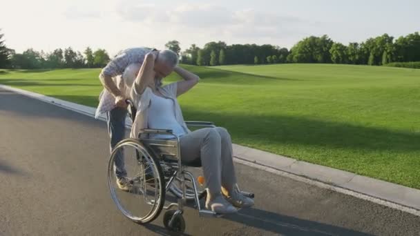 Äldre par med fru i rullstol på en promenad — Stockvideo