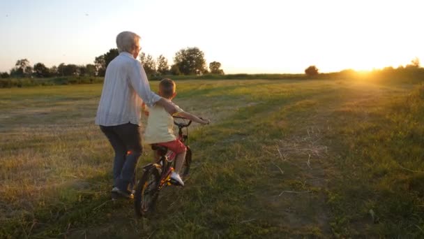 Back view of boy learning to ride bike with granny — Stock Video