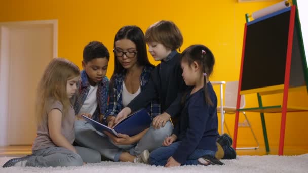 Preschool teacher reading a book to diverse kids — Stock Video