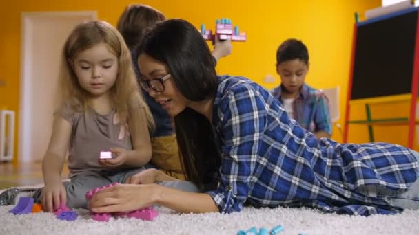 Öğretmen çocuk inşaat oyuncak blokları ile yardımcı olur — Stok video