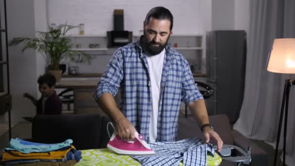 Alleinerziehender schöner Vater bügelt Kleidung zu Hause — Stockvideo
