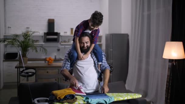 Caring father with son on shoulder ironing clothes — Stock Video
