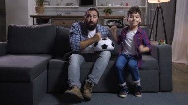 Baba ve karışık yarış oğlu izlerken spor tv ve tezahürat futbol takımı heyecanlı. Çocuk TV footaball oyun yayın sırasında bir hedef eksik sonra olumsuz duyguları ifade ile hayal kırıklığına baba.