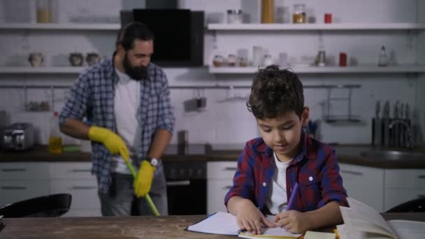 Lindo filho fazendo lição de casa enquanto o pai esfregando chão — Vídeo de Stock