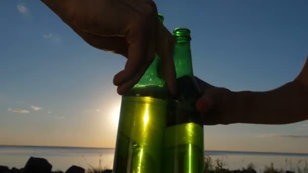 Primer plano manos tostando botellas de cerveza al atardecer — Vídeos de Stock